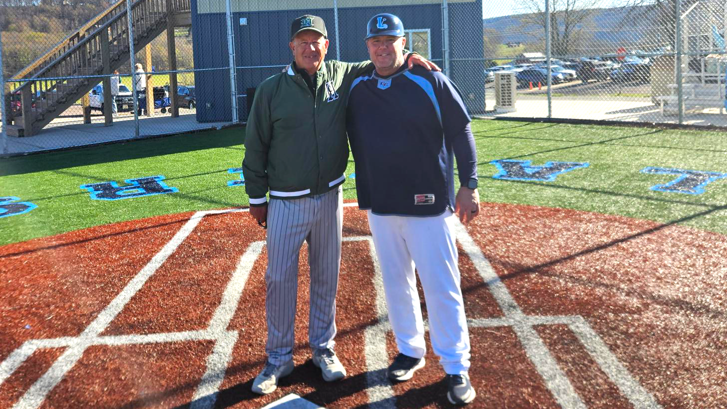 two baseball coaches stand at home plate celebrating milestone wins together